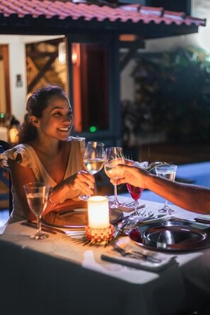 A dining table with a candle, wine glasses, and a person toasting.