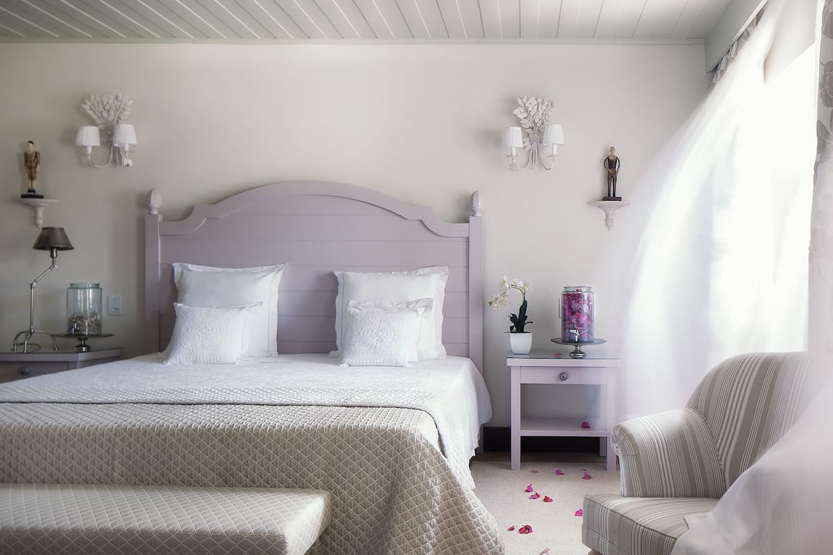 A bedroom with a large bed, bedside tables, a chair, and decorative wall sconces.