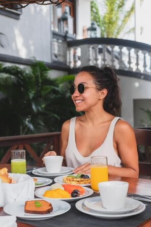 A person seated at an outdoor table with a meal consisting of various dishes, a glass of orange juice, and a cup.