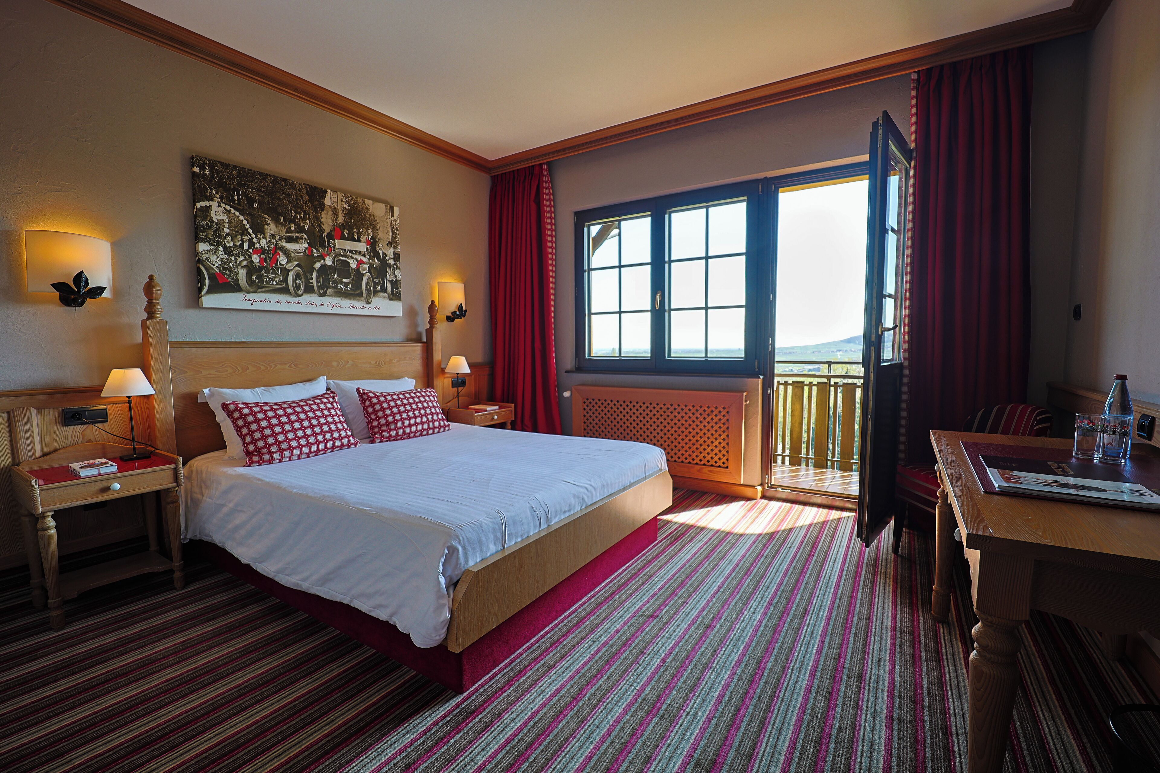 Ein Hotelzimmer mit einem großen Bett, einem Schreibtisch, einem Stuhl, einem Fenster mit Vorhängen und einem Bild an der Wand.