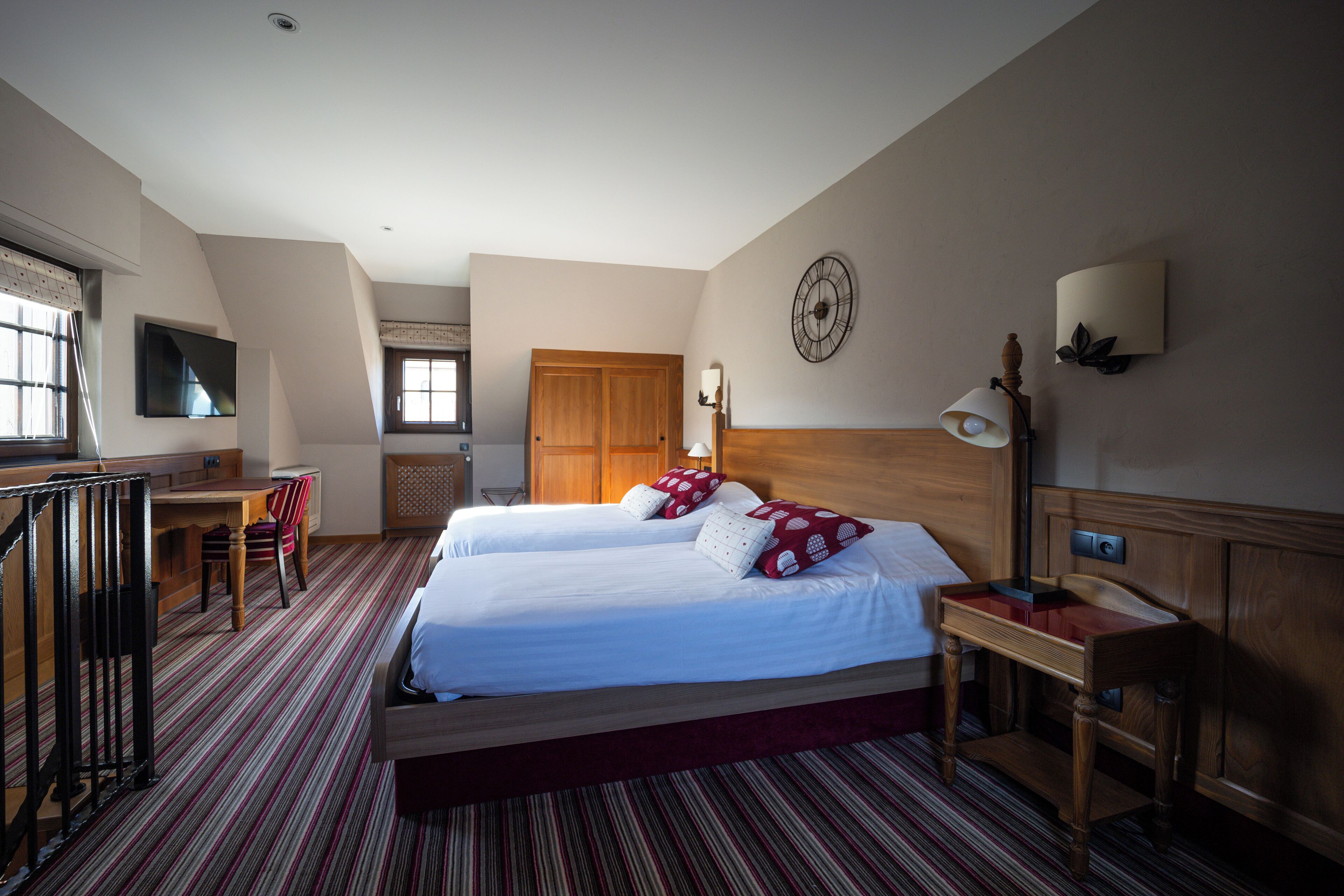 A hotel room with two beds, a desk, a chair, a TV, a clock, and a lamp.