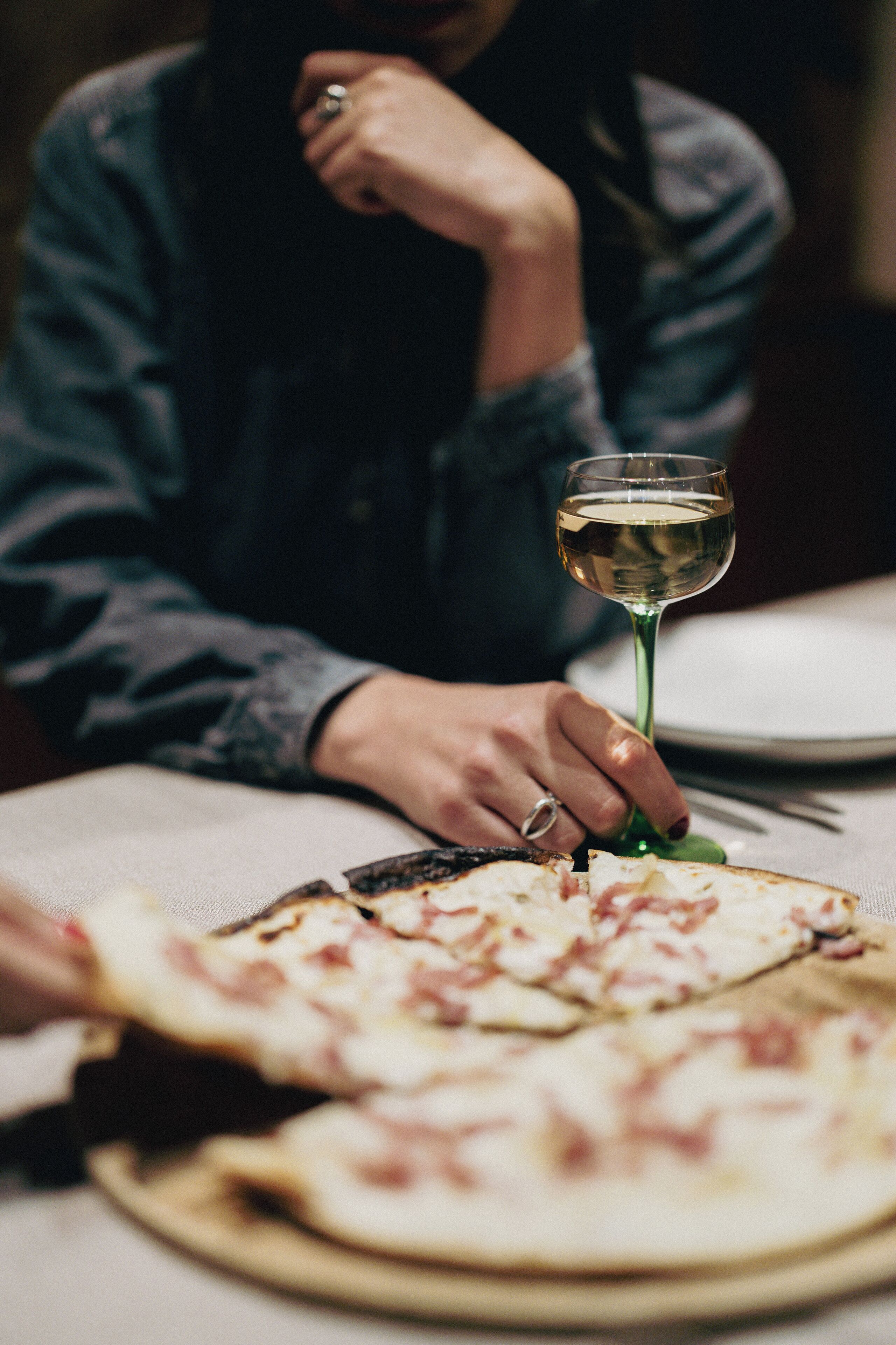 A person sitting at a table with a pizza and a glass of white wine.