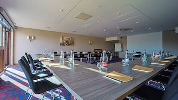 Un salón de conferencias con una larga mesa, sillas, botellas de agua y una pantalla de proyector.