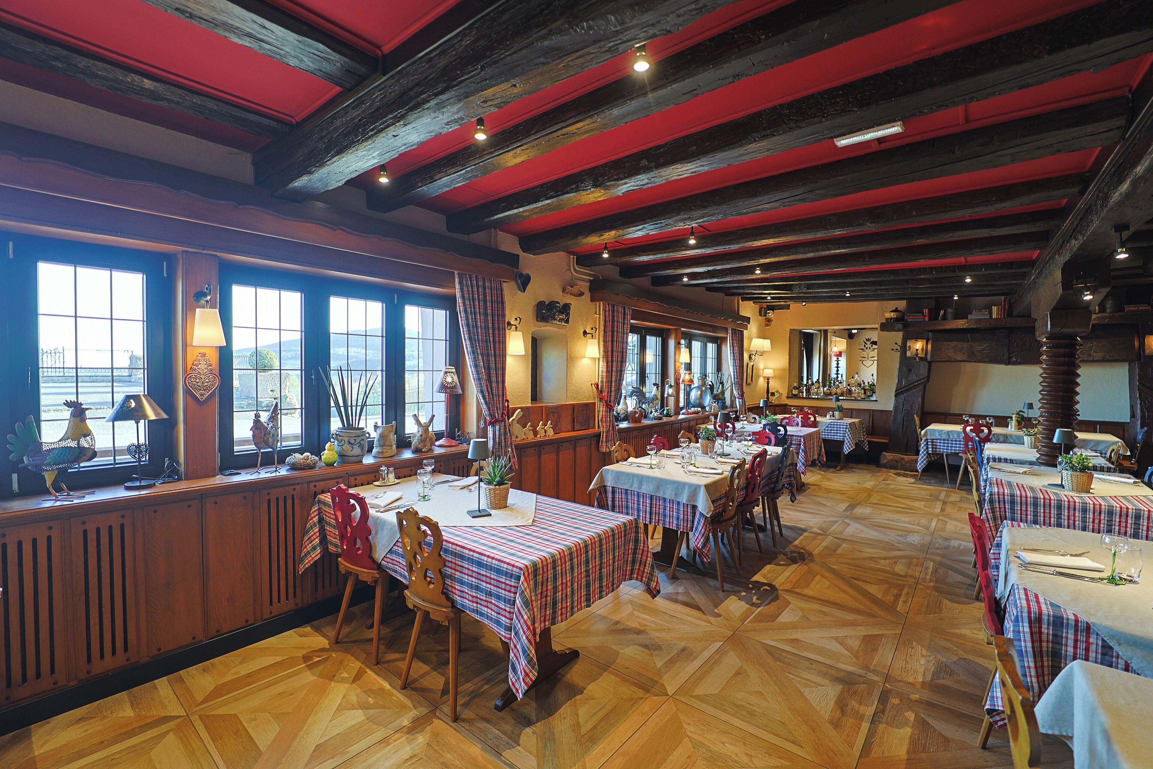 A restaurant with wooden floors and red beams on the ceiling, featuring multiple tables with plaid tablecloths and chairs.