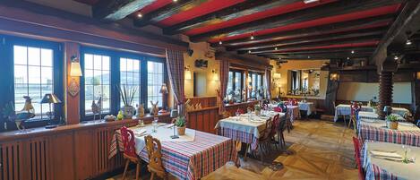 A restaurant with wooden floors and red beams on the ceiling, featuring multiple tables with plaid tablecloths and chairs.