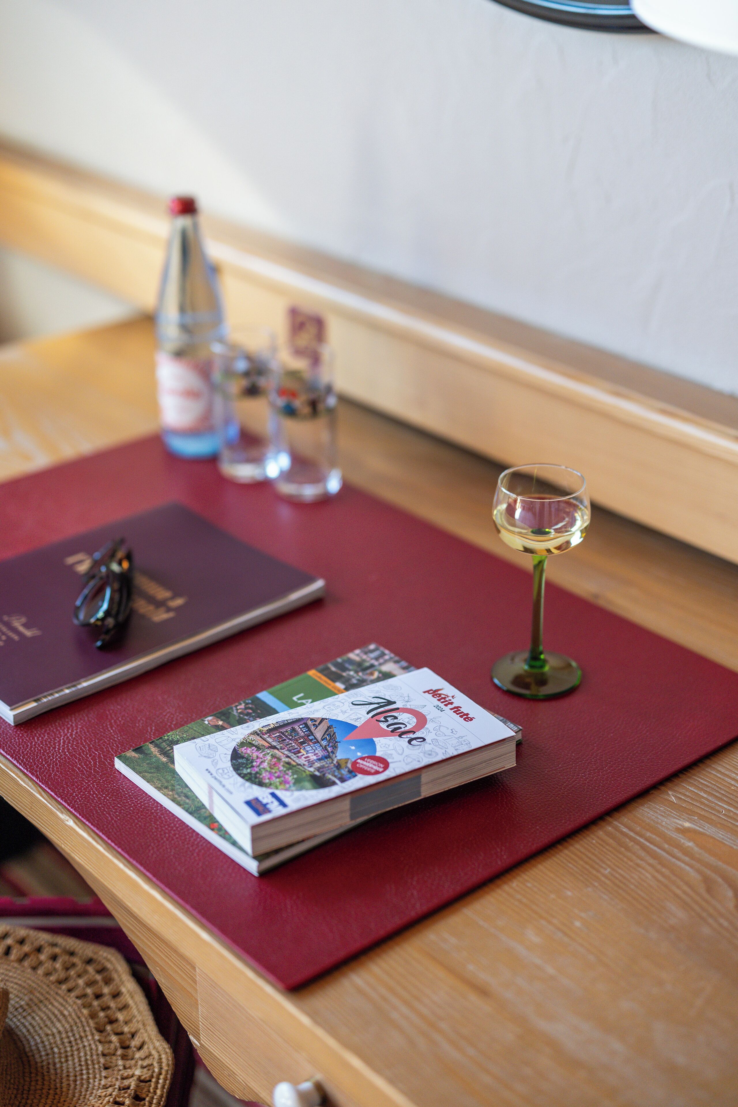 A table with a red mat, a book, a pair of glasses, a glass of wine, and a bottle of water.