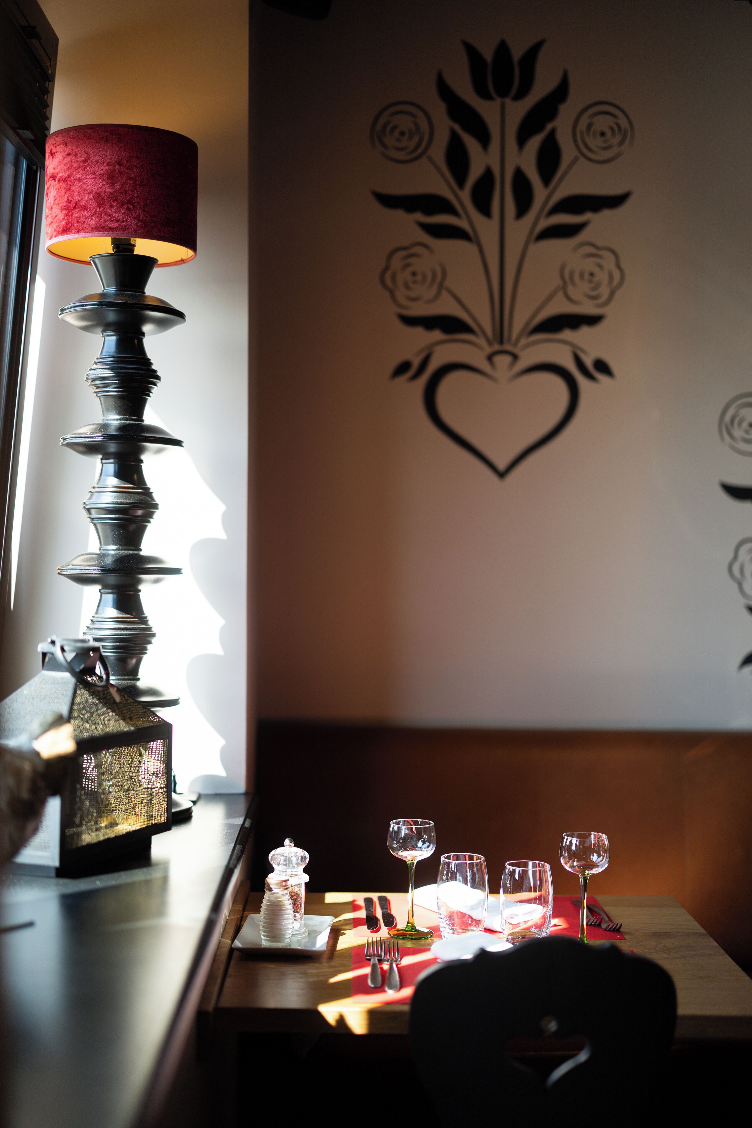 A dining table with wine glasses and a candle, a lamp, and a decorative wall with a floral design.