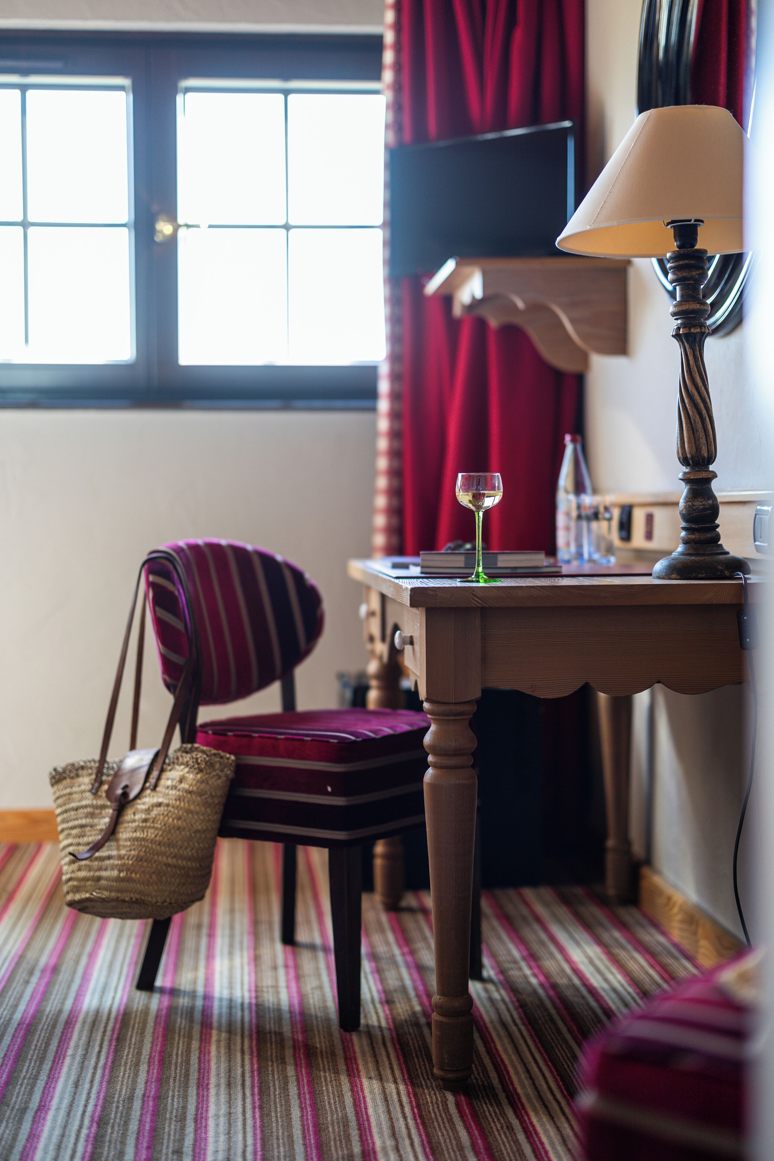 Une pièce avec un tapis à rayures, une table en bois sur laquelle se trouve une lampe, une chaise, un verre de vin et, au fond, un téléviseur.