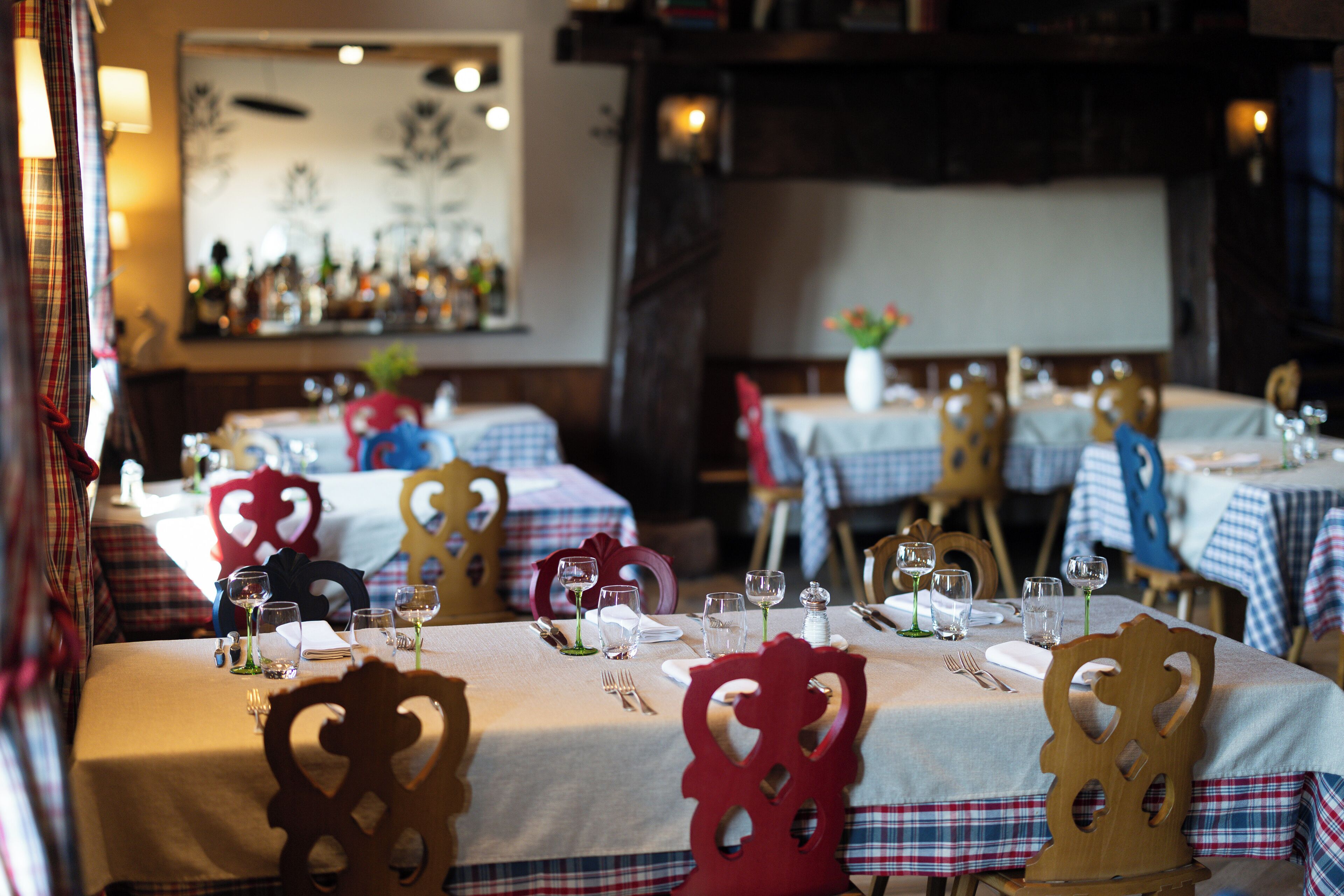 Ein Restaurant mit gedeckten Tischen, mit karierten Tischdecken und Stühlen aus Holz mit ausgeschnittenen Verzierungen.