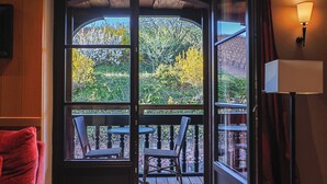 A room with a view of a garden through a glass door, a red sofa, a striped carpet, and a lamp on the wall. - Hotel Arnold (Itterswiller)