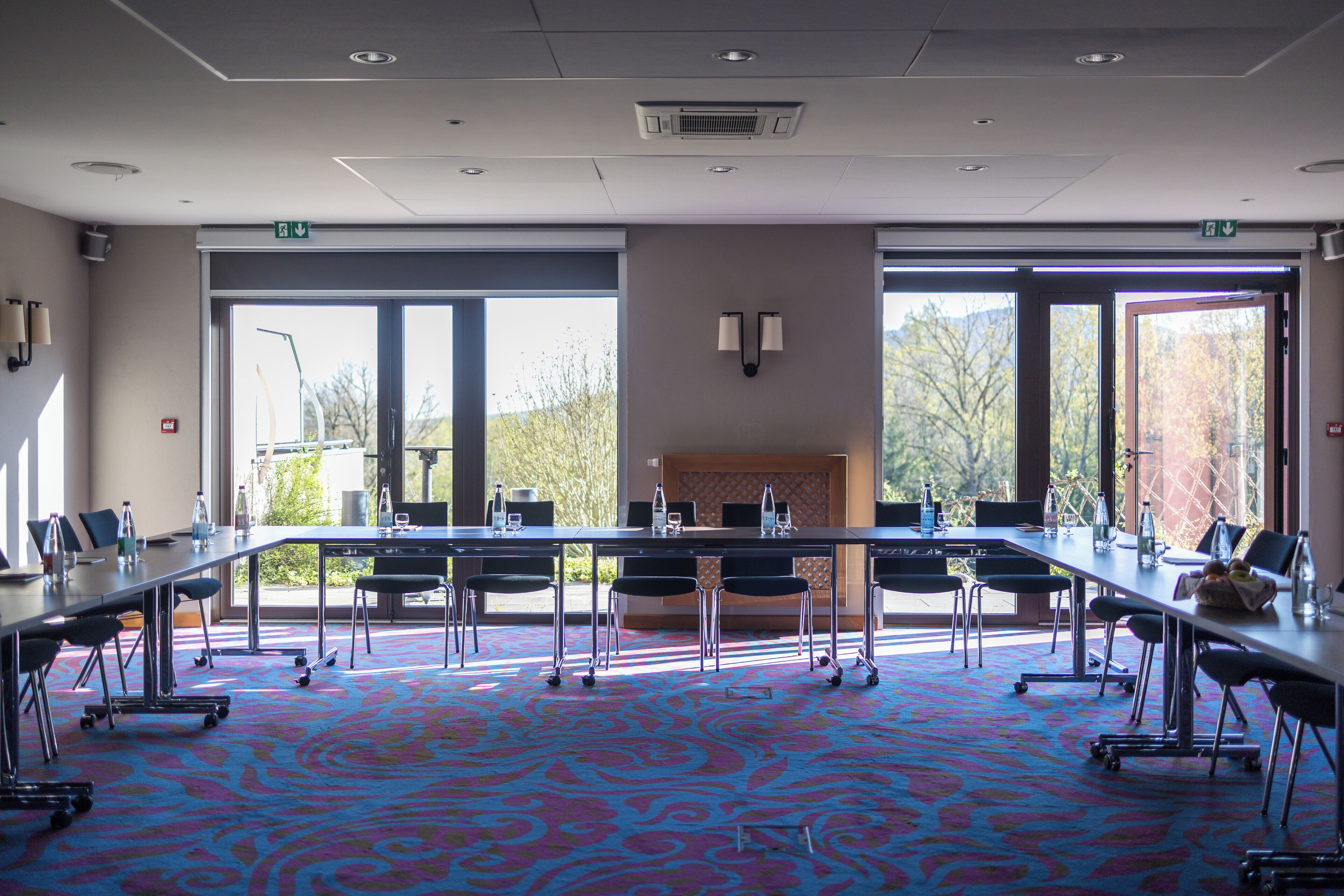 A conference room with a large table, chairs, and a patterned carpet.