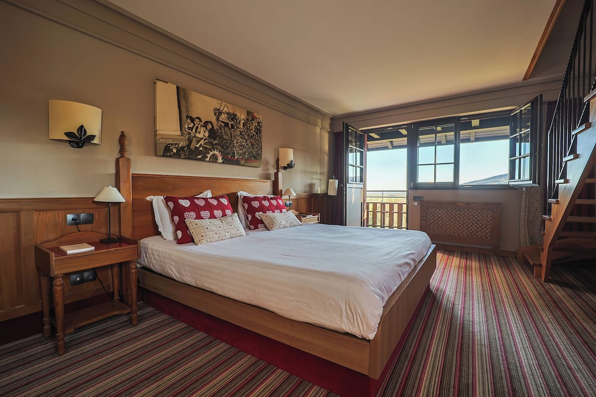 A large bed with a wooden headboard, a nightstand with a lamp, and a red-striped carpet.