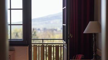 Una habitación de hotel con balcón, una cama, una mesa con lámpara y un tapete a rayas.