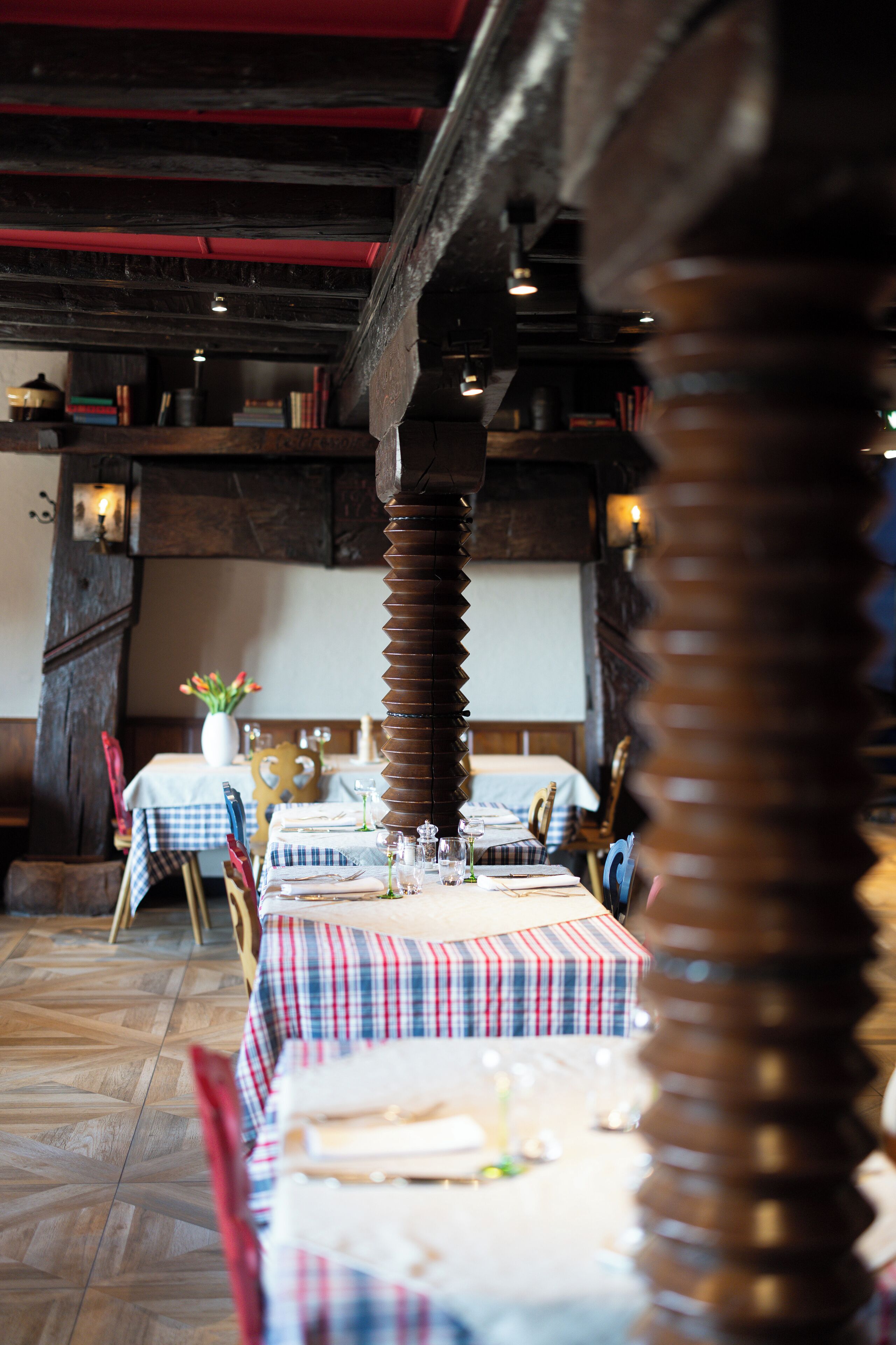Un restaurante con vigas de madera y mantel a cuadros. Las mesas están dispuestas con platos, vasos y cubiertos.
