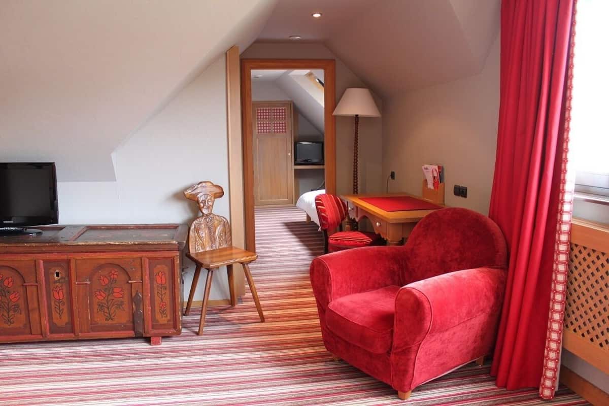A compact room with a television, a wooden cabinet, a red chair, a small table, and a red curtain.