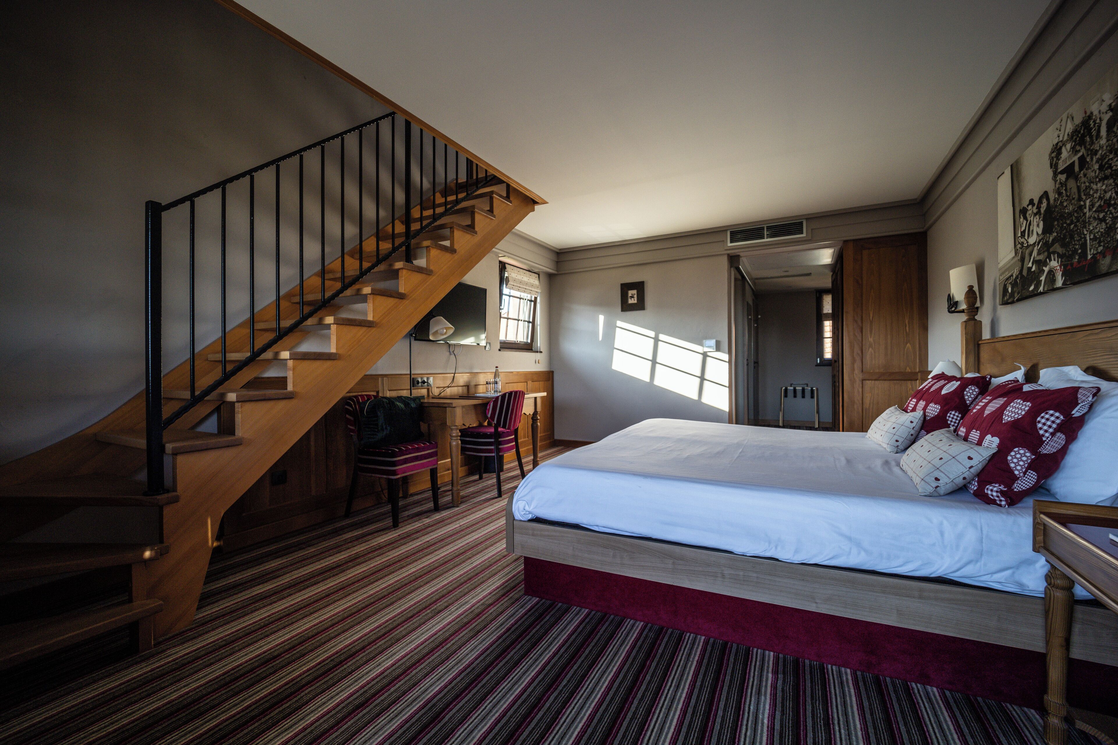 Un dormitorio con escalera de madera, una cama grande con muchos almohadones, un escritorio y una silla.