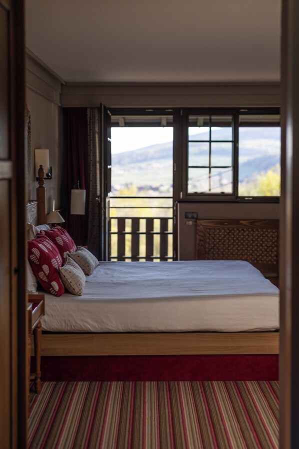 A bedroom with a large bed, a view of the outdoors through an open door, and a balcony with a railing.