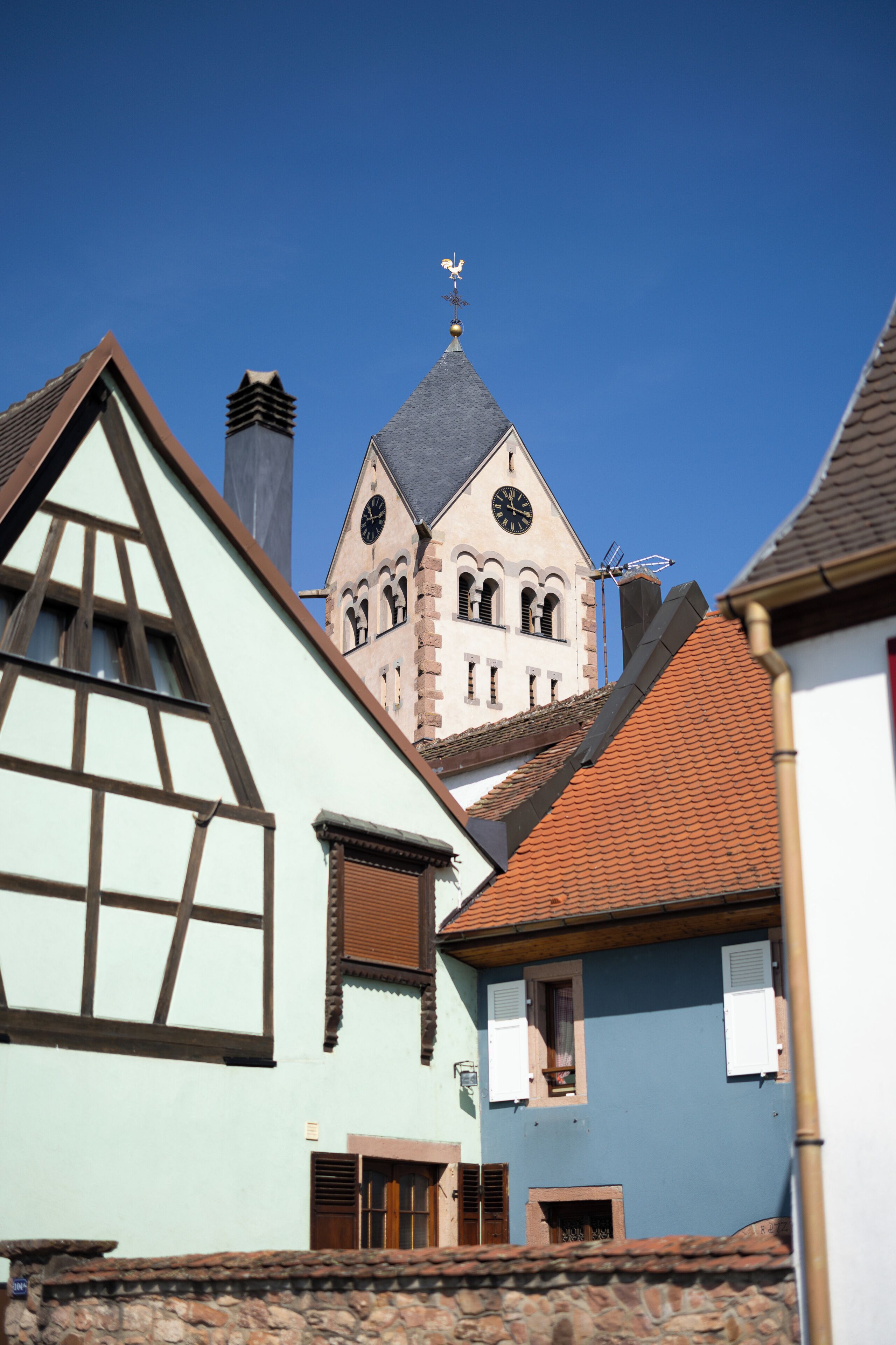 A traditional European building with a prominent clock tower, steeply pitched roofs, and a clear blue sky.