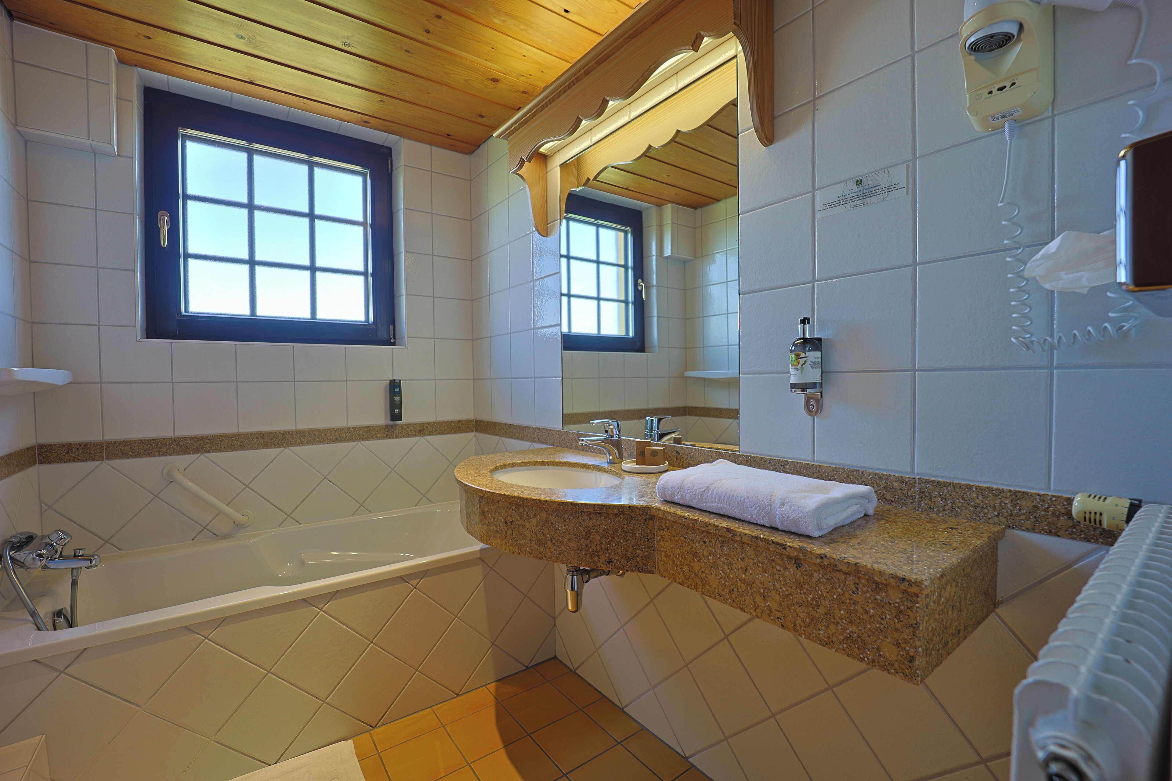 A bathroom with a bathtub, a sink, a mirror, and a window.