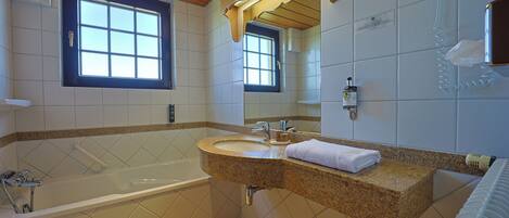 A bathroom with a bathtub, a sink, a mirror, and a window.