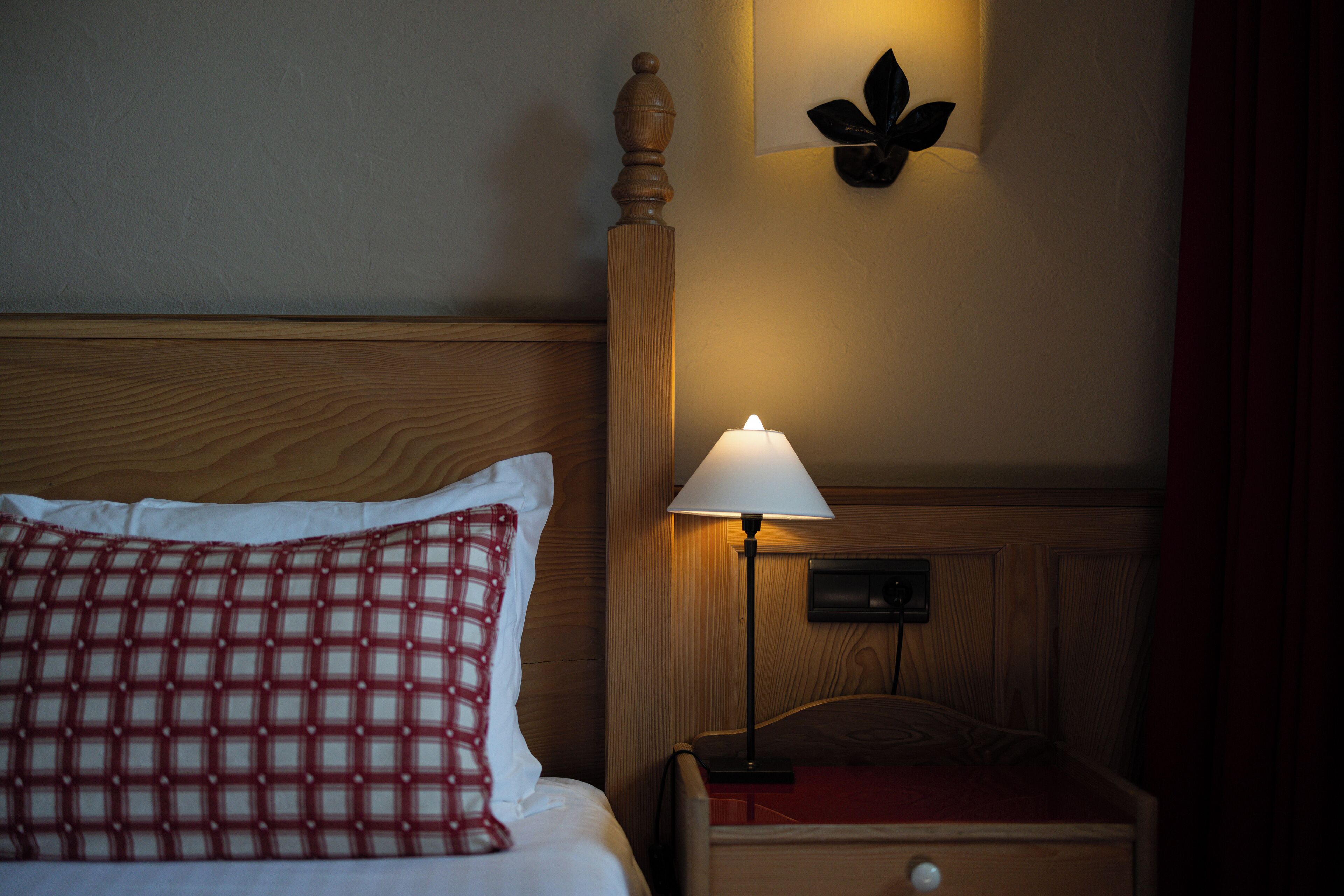 Un lit bien fait, avec un oreiller à carreaux, une lampe de chevet et un luminaire fixé au mur.