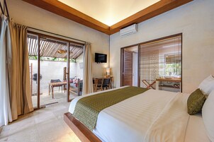 Habitación de hotel con cama, escritorio, silla, televisión y puerta corrediza de vidrio que da a un área exterior.