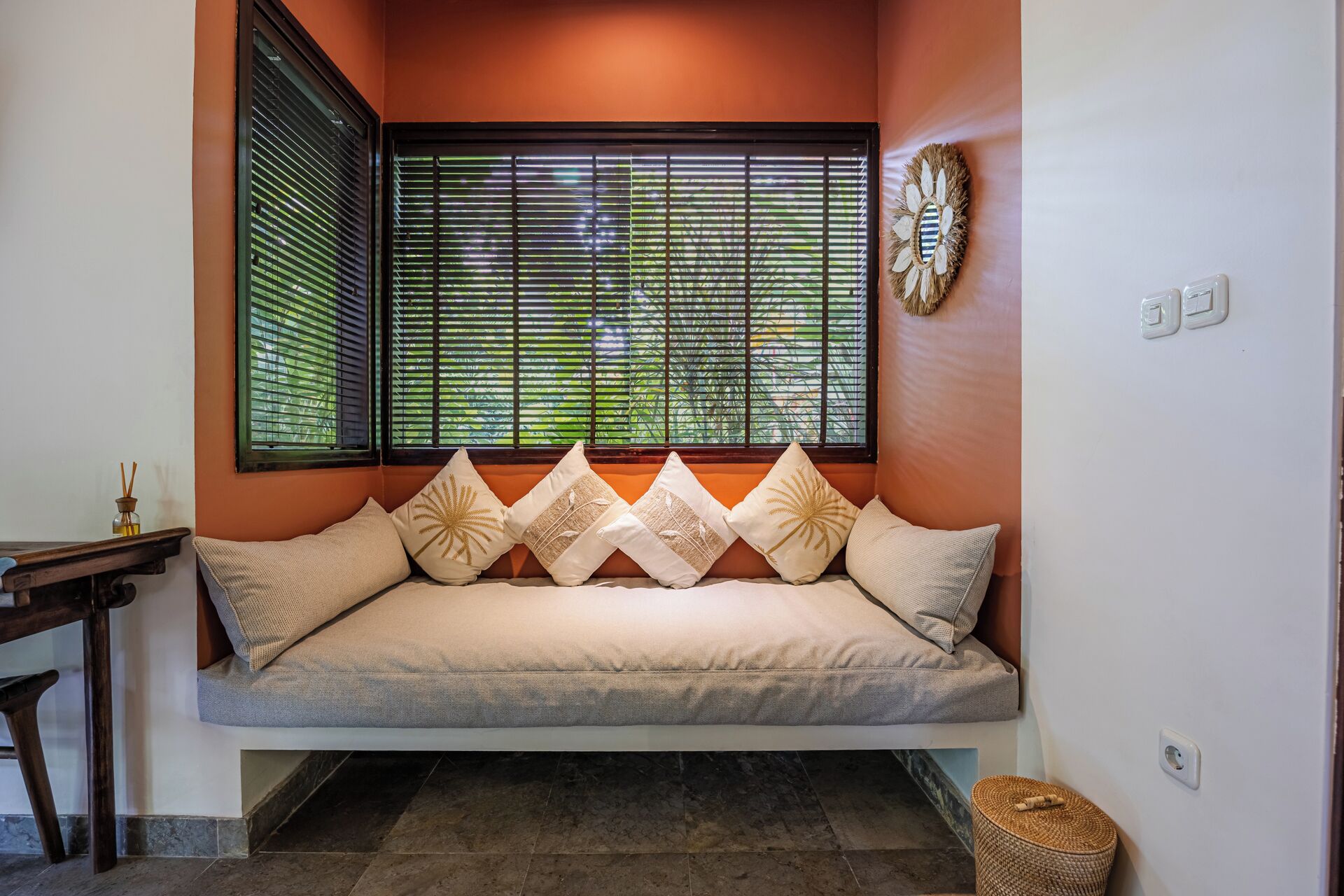 A room with a sofa against a wall, a window with blinds, a small table, and a decorative item on the wall.