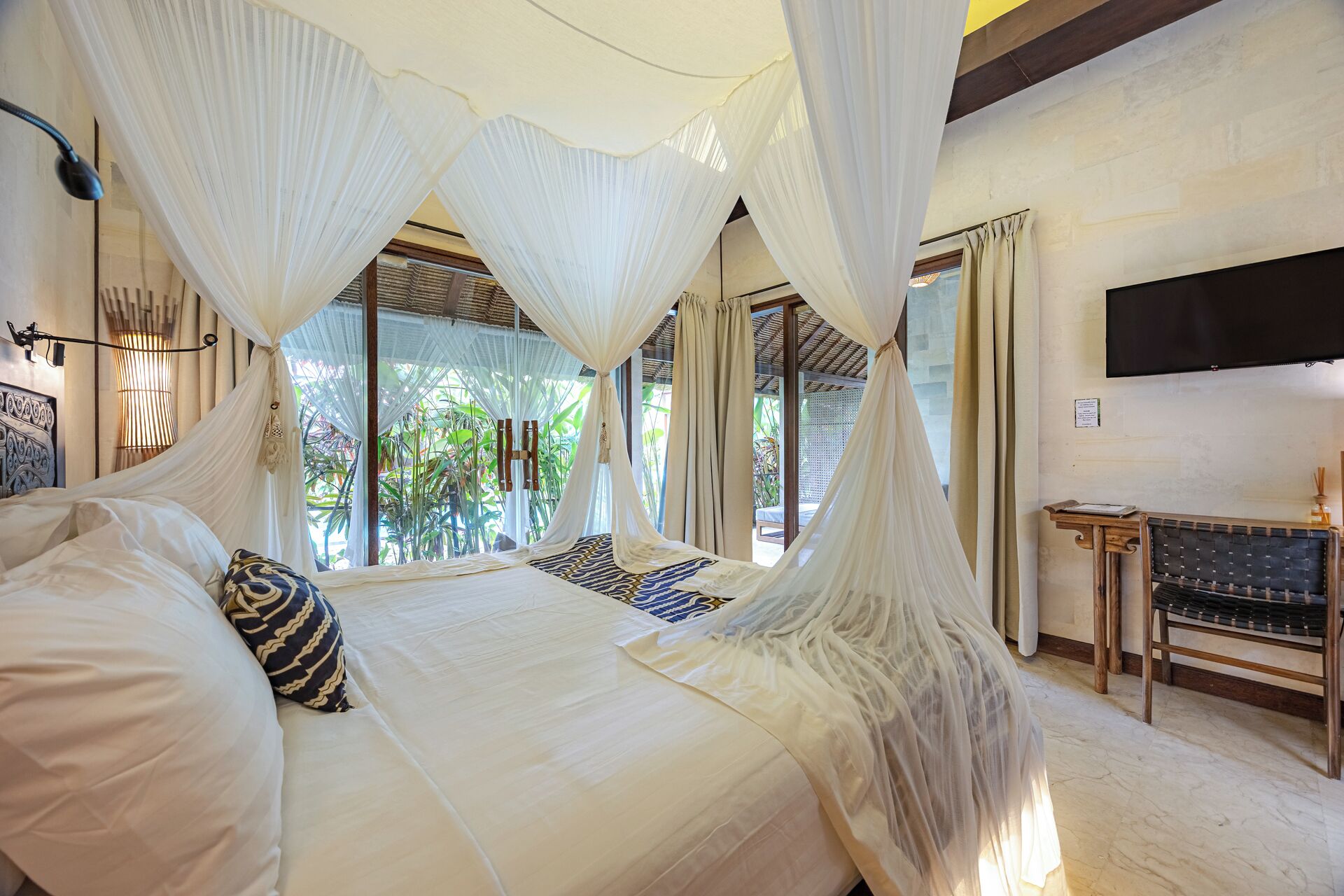 A bedroom with a canopy bed, a desk, and a view of greenery outside.