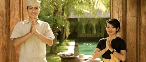 A man and a woman standing in a wooden doorway with a pool and palm trees in the background.