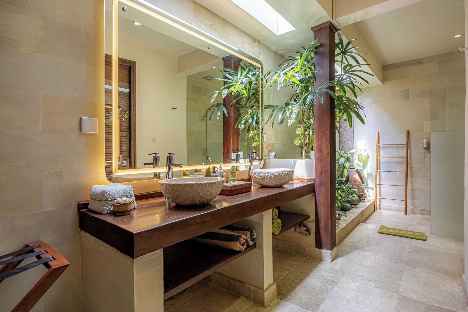 Un baño con un tocador de madera, dos espejos grandes y una planta en maceta grande.