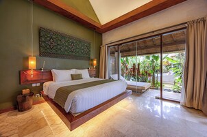 A spacious bedroom with a large bed, wooden headboard, and a view of lush greenery through a sliding glass door.