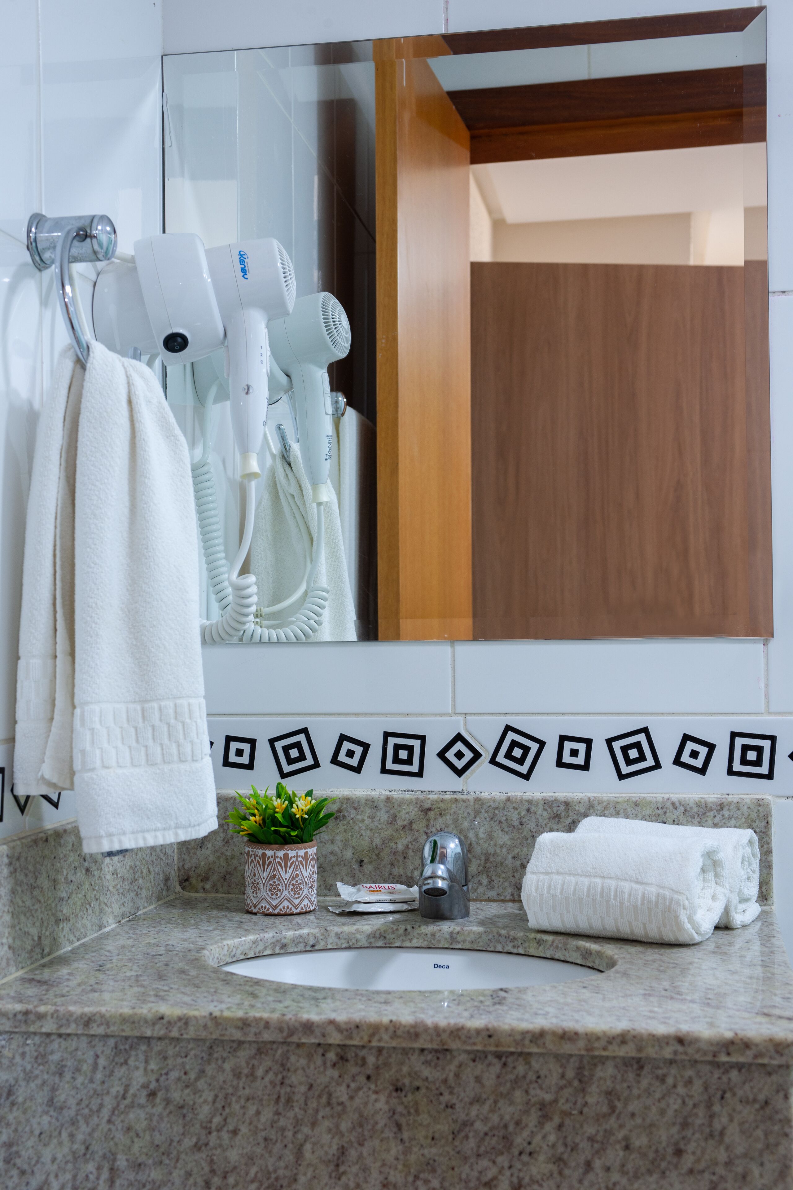 A bathroom with a granite countertop, a sink, a towel rack with white towels, a hairdryer, and a small potted plant.