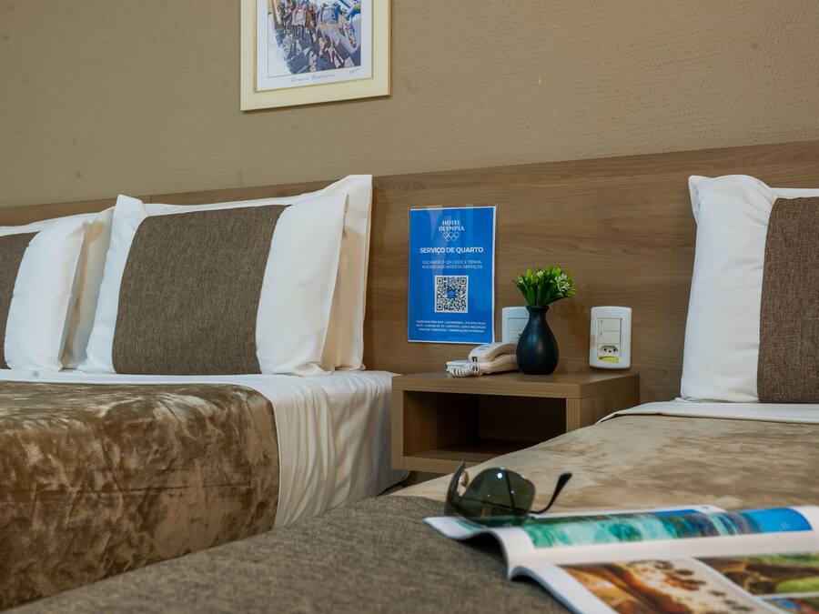 A hotel room with two beds, a nightstand with a lamp, a framed photo on the wall, and a QR code sign.