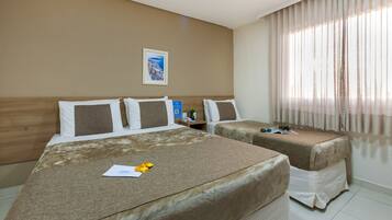 Habitación de hotel con dos camas, una mesita de noche, un cuadro en la pared y una ventana con cortinas translúcidas.