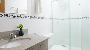 Un baño moderno con lavamanos de granito, un espejo, inodoro y cabina de ducha de vidrio.