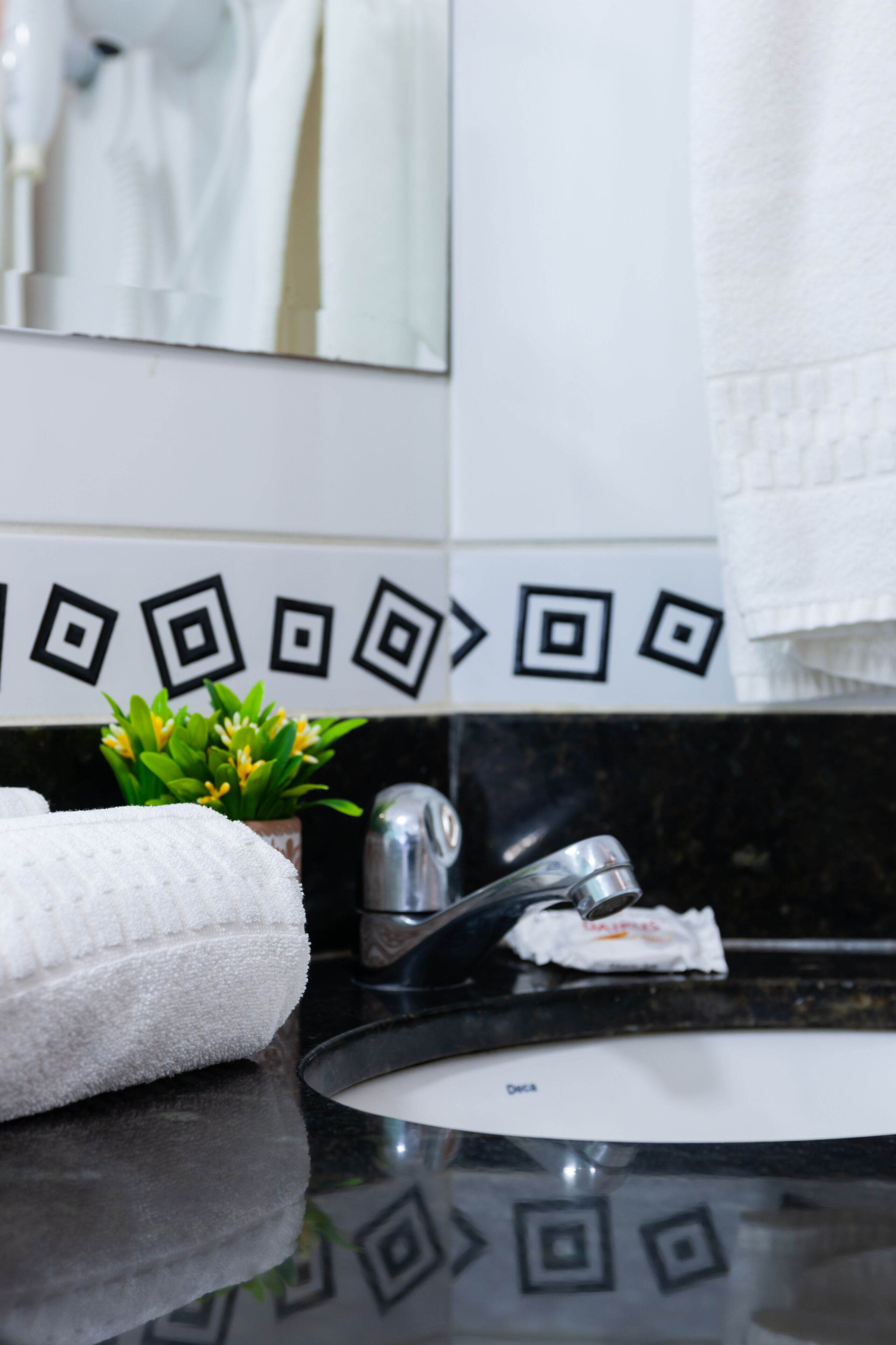 A bathroom with a black countertop, a white sink, and a mirror above it. There is a towel on the counter and a small plant beside the mirror.