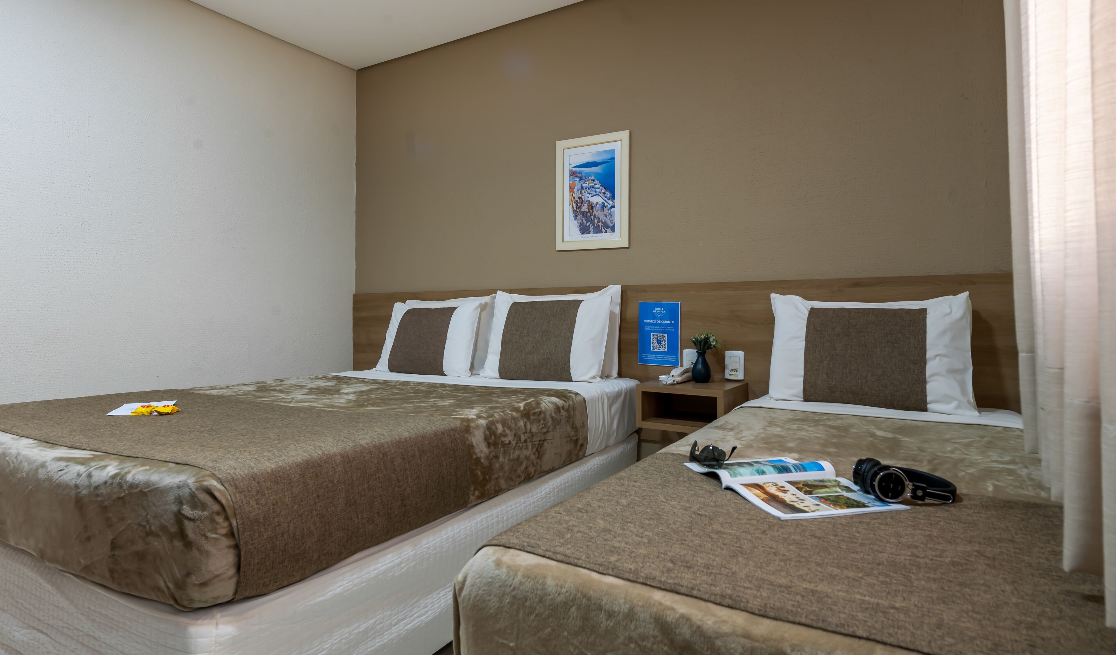 Quarto de hotel com duas camas, uma mesinha de cabeceira com telefone e um vaso, e um quadro na parede.