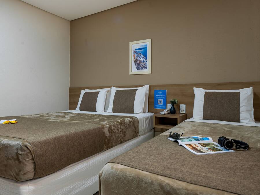 Hotellihuone, jossa on kaksi sänkyä, yöpöytä, jossa on puhelin ja maljakko, sekä seinällä oleva kehystetty kuva.