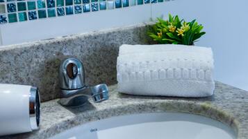 Un baño con encimera de granito, un lavabo blanco, una toalla, un grifo y una planta pequeña.