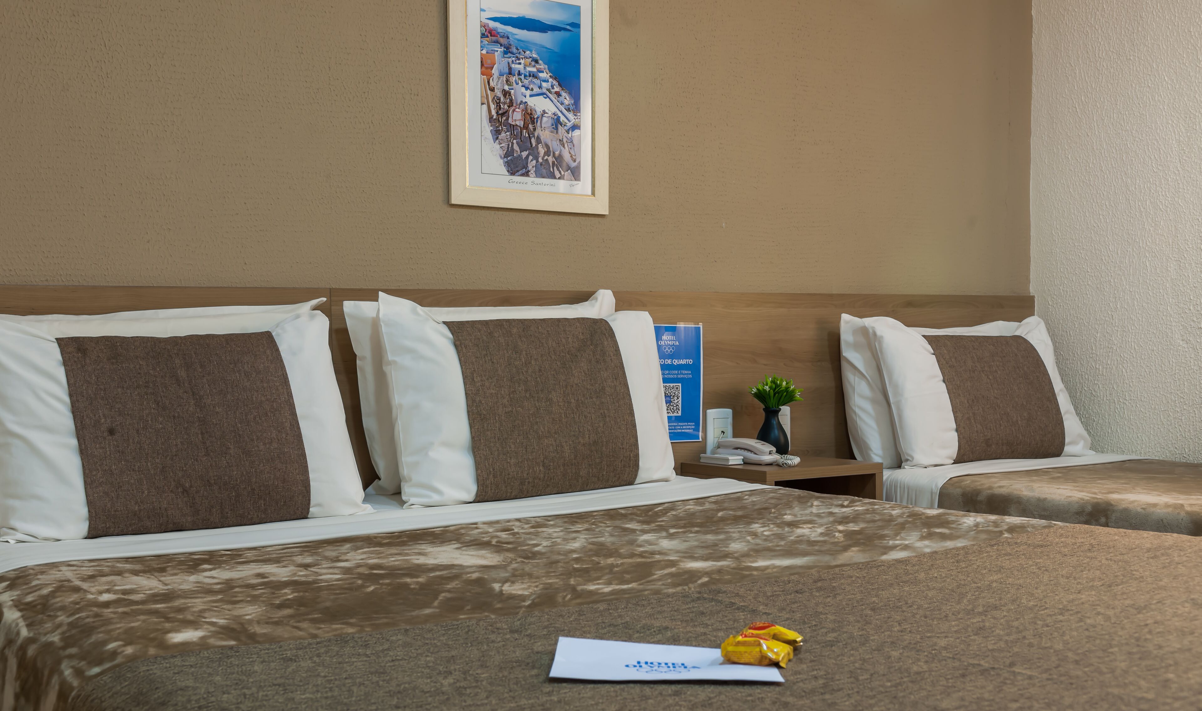 Habitación de hotel con dos camas, una mesita de noche con un teléfono y una planta pequeña, y un cuadro en la pared.