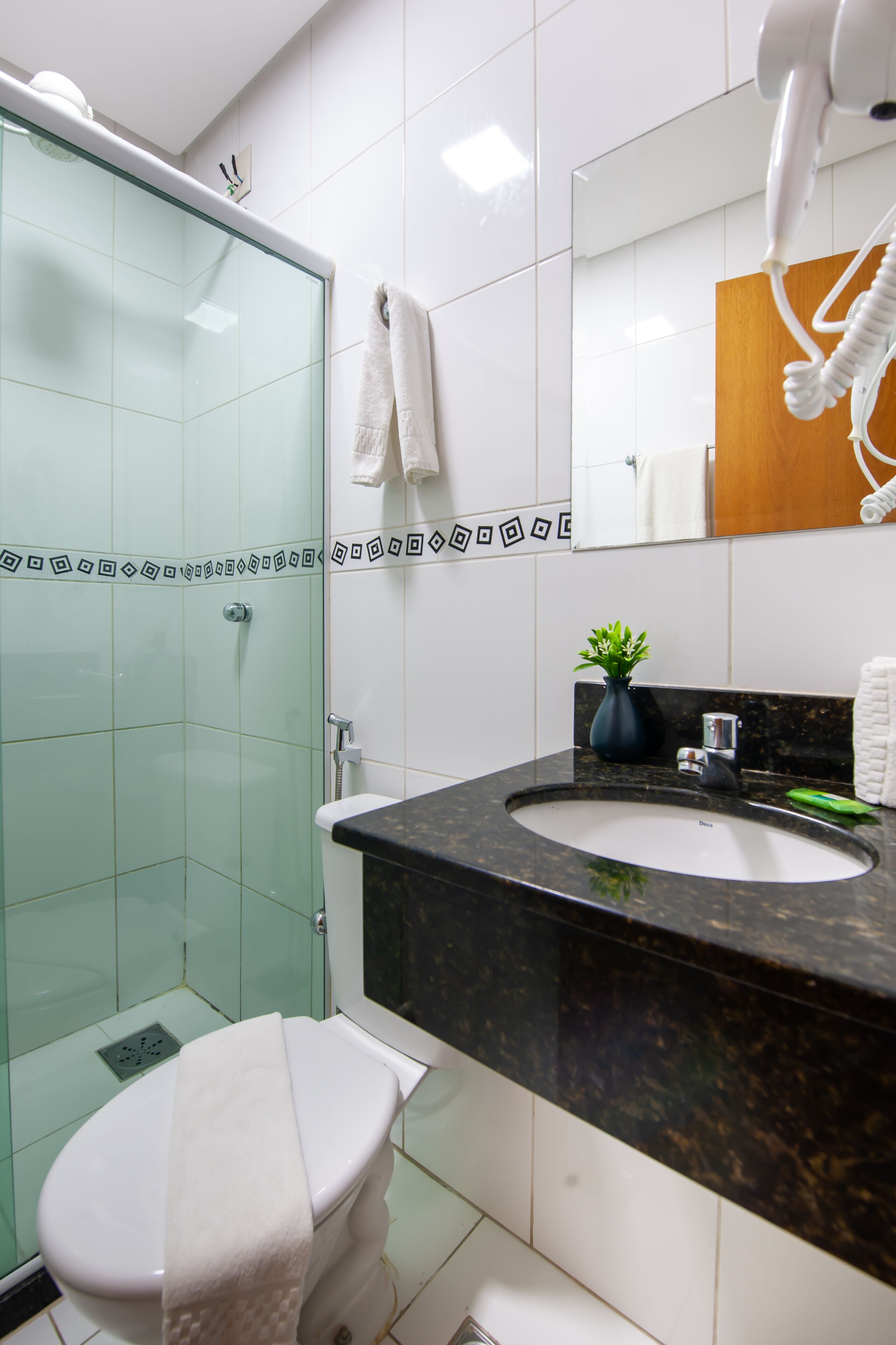 Un baño moderno con cabina de ducha de vidrio, inodoro blanco, lavabo de mármol negro y un espejo con una toalla colgada.