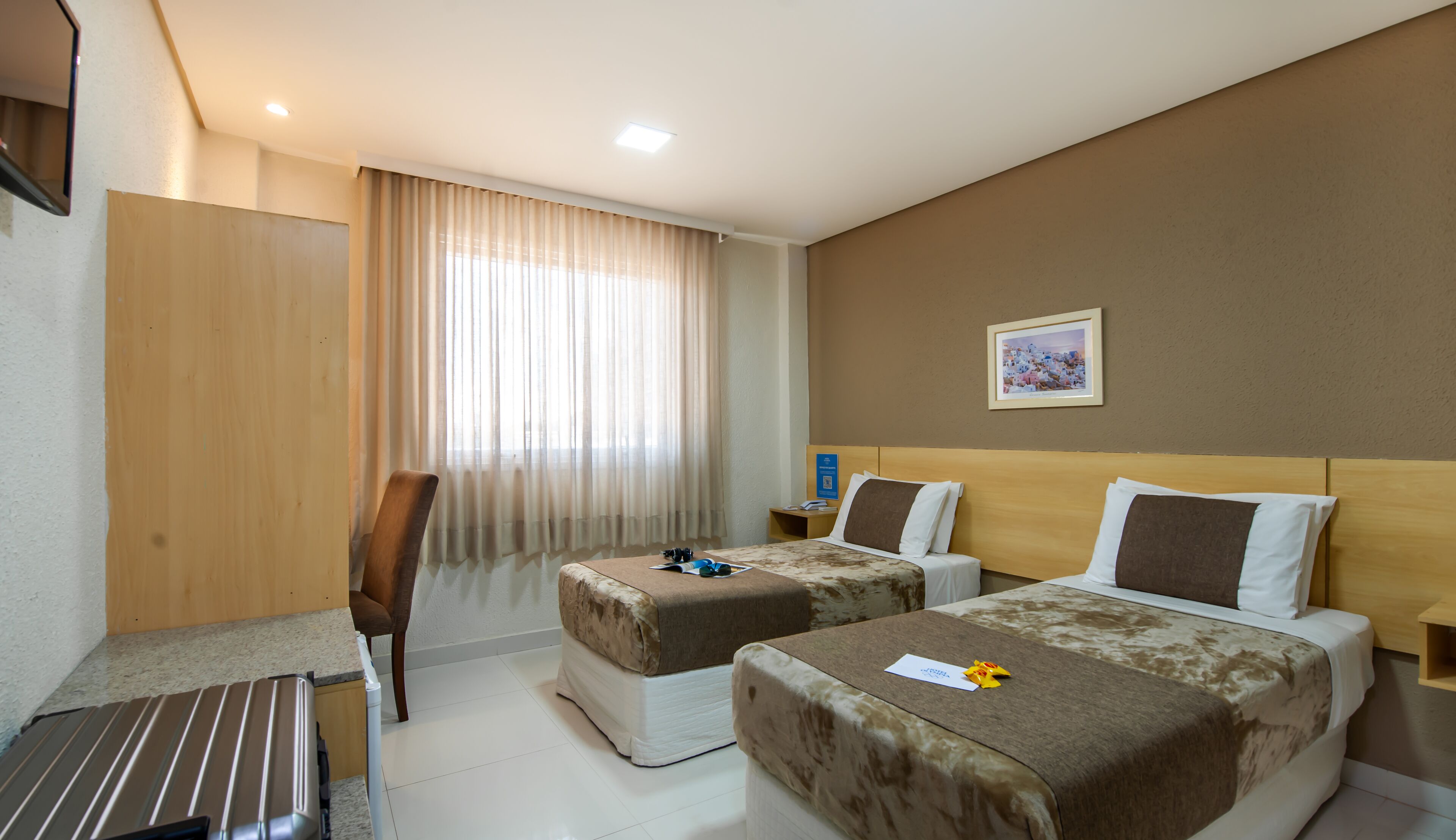 A hotel room with two beds, a desk, a chair, and a window with curtains.