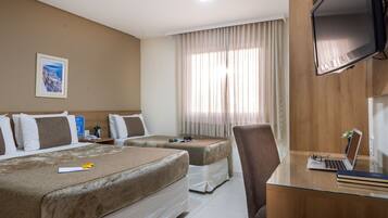 A hotel room with two beds, a desk with a laptop, a chair, a TV, and a window with curtains.