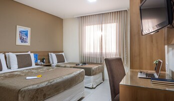 Habitación de hotel con dos camas, un escritorio con una computadora portátil, una silla, un televisor y una ventana con cortinas.
