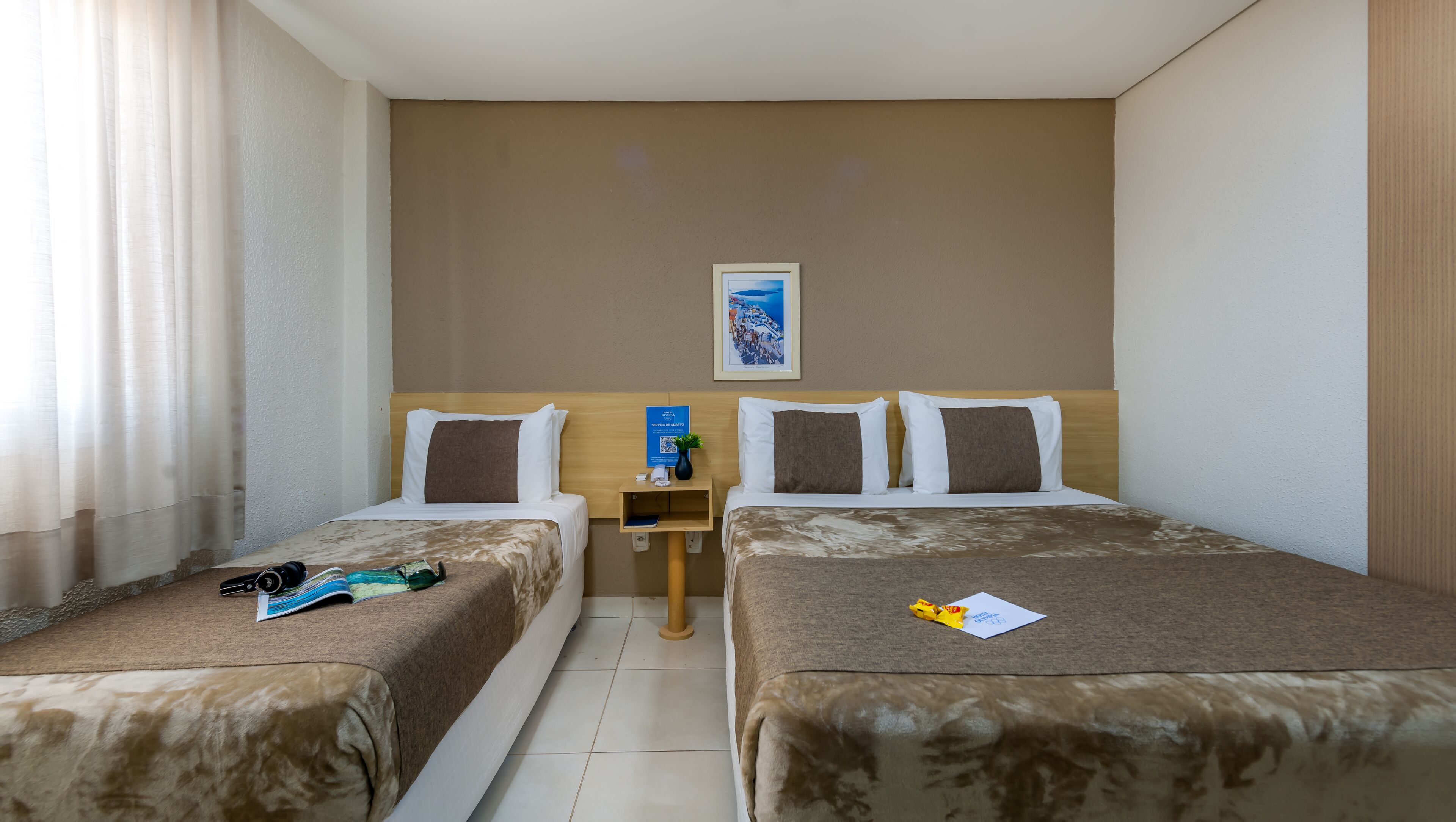 A hotel room with two beds, a small table, and a framed picture on the wall.