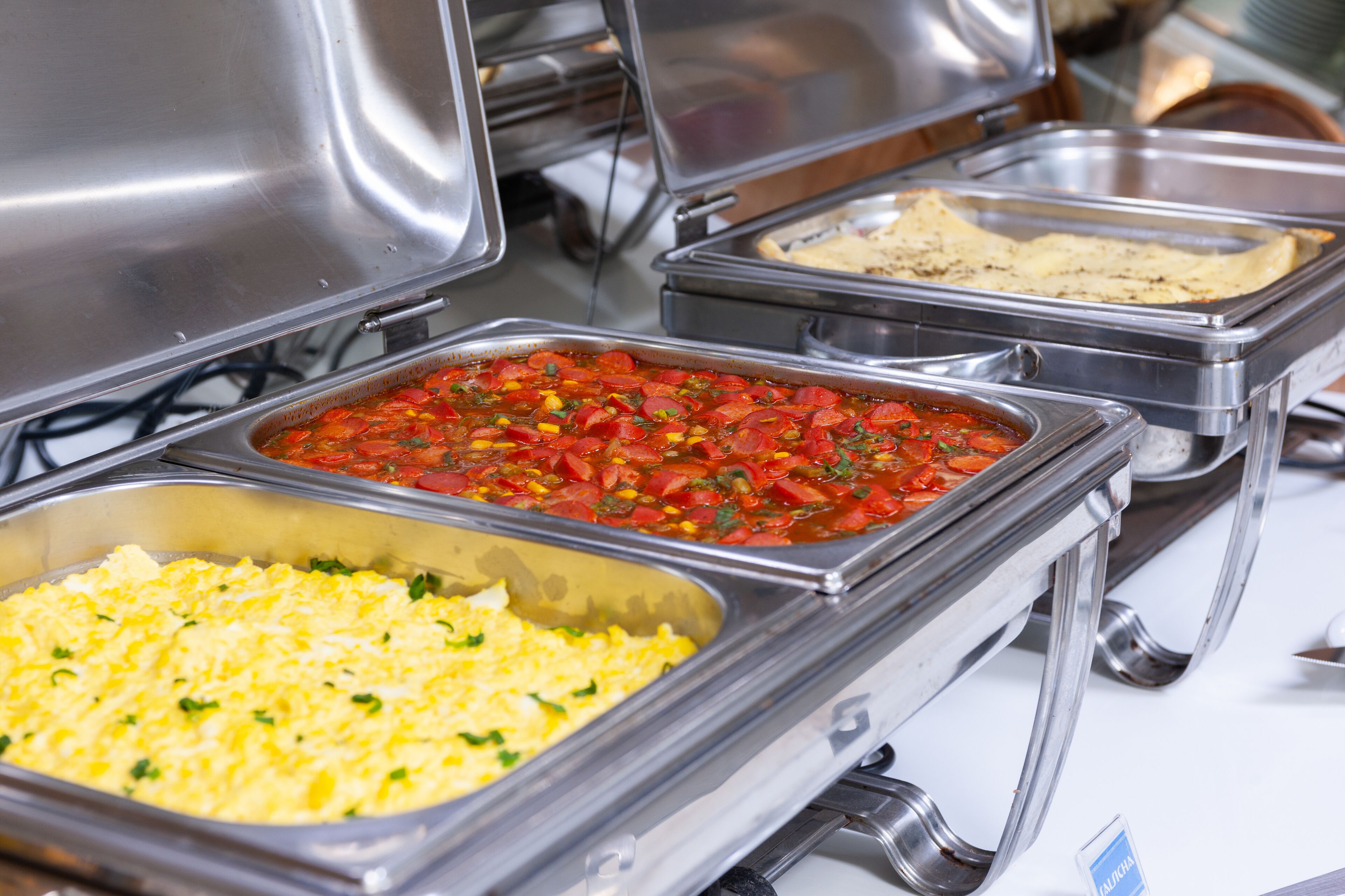 A buffet with various food items including scrambled eggs, a tomato-based dish, and a tortilla dish.