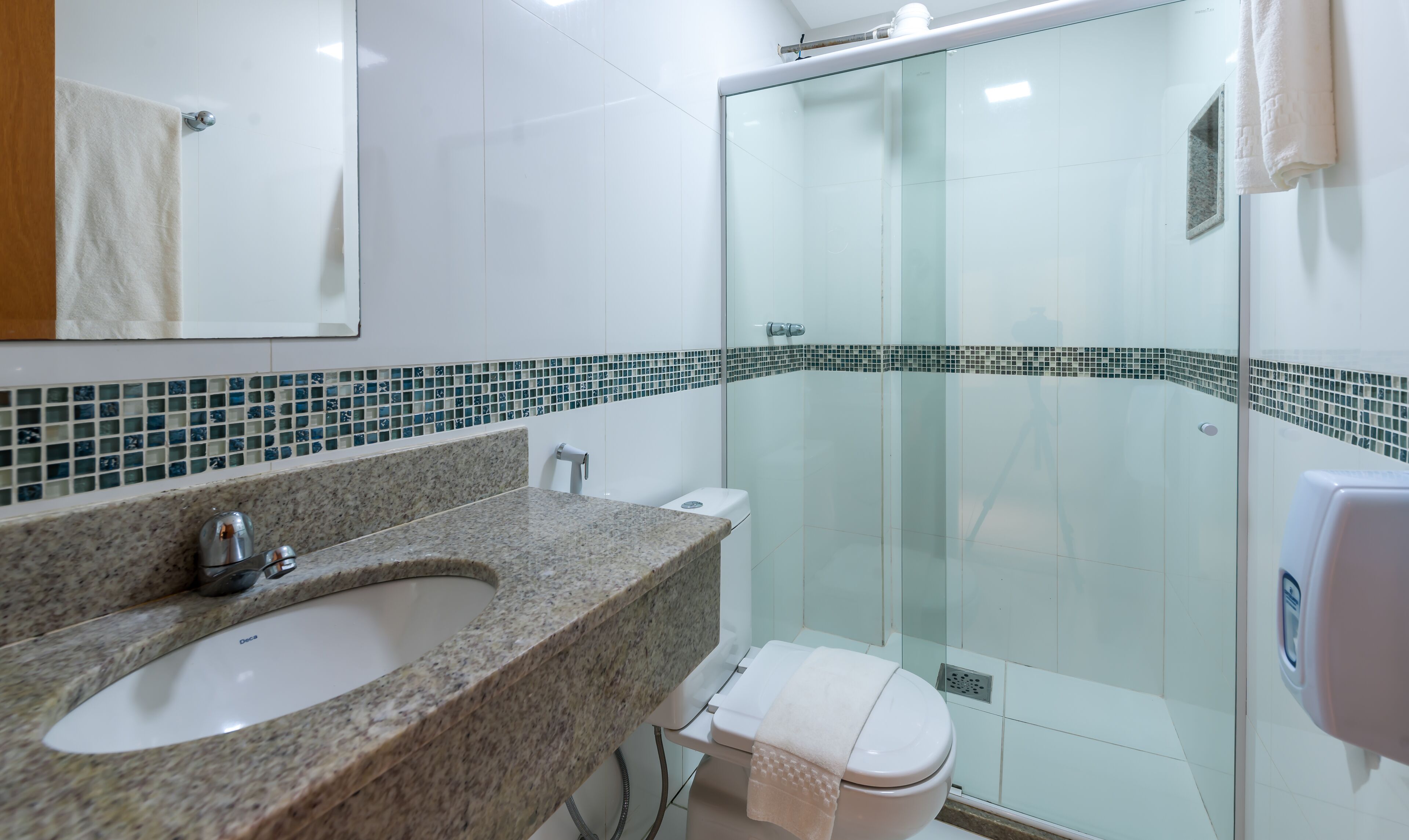 A modern bathroom with a granite countertop sink, a toilet, and a glass shower enclosure.