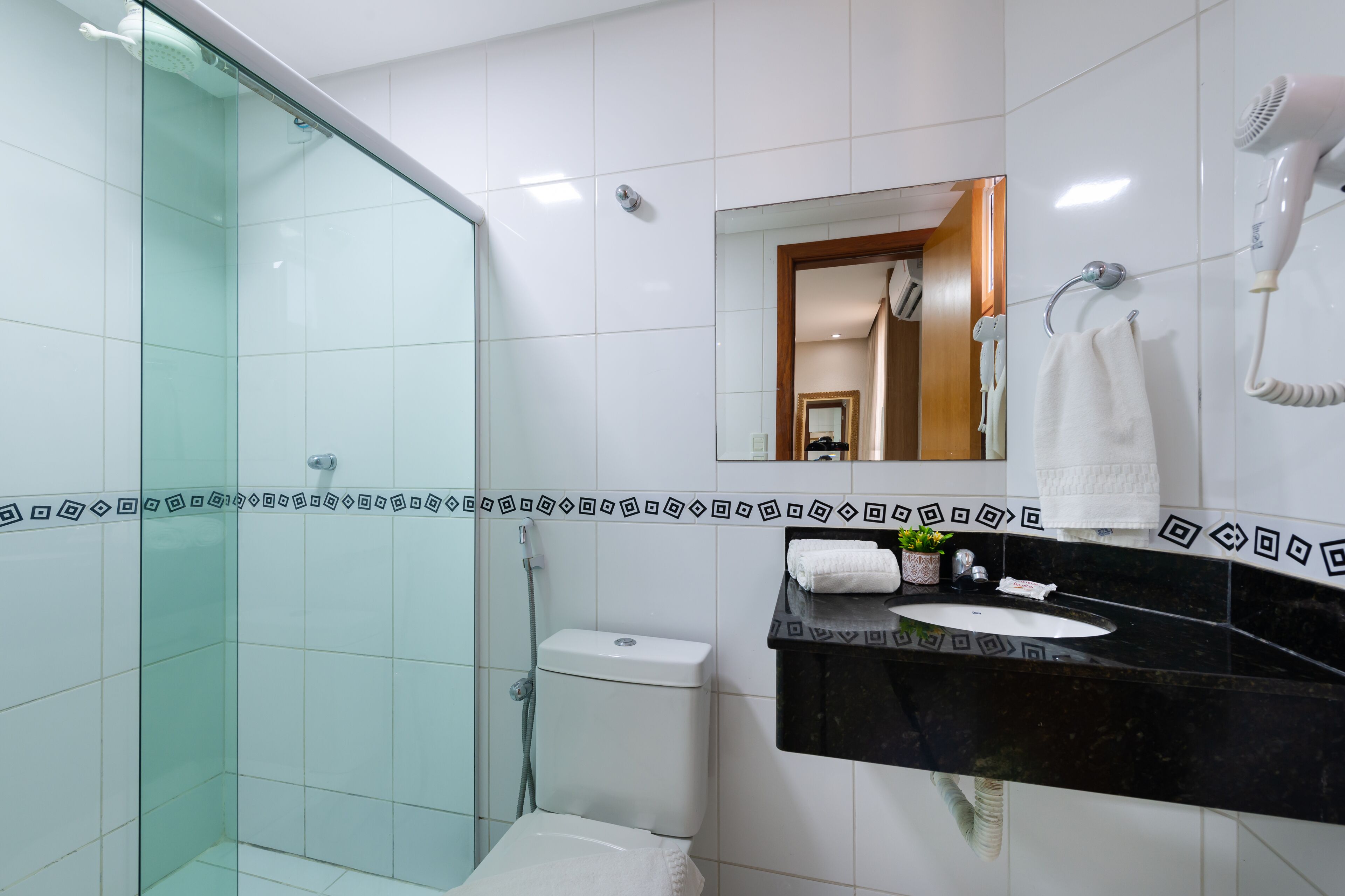 A modern bathroom with a glass shower enclosure, a black countertop sink, a white toilet, and a mirror above the sink.
