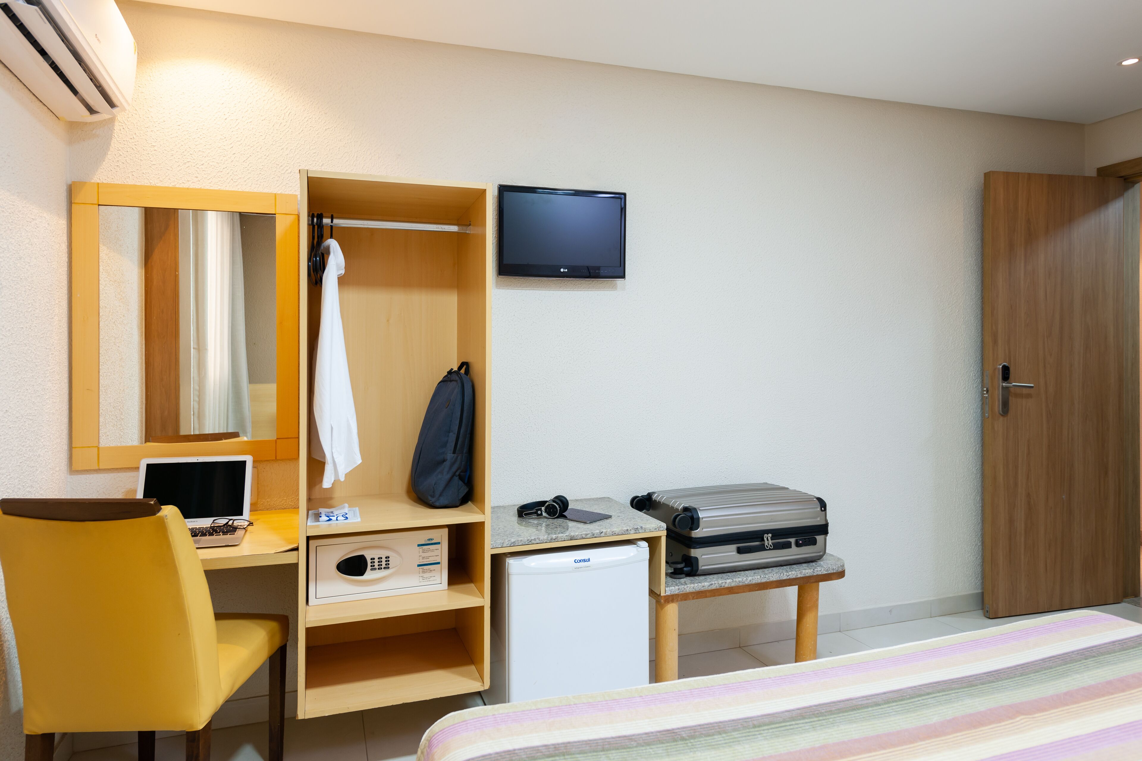 Une chambre d’hôtel comprenant un lit, un bureau avec un ordinateur portable, un petit réfrigérateur, une télévision et une armoire.