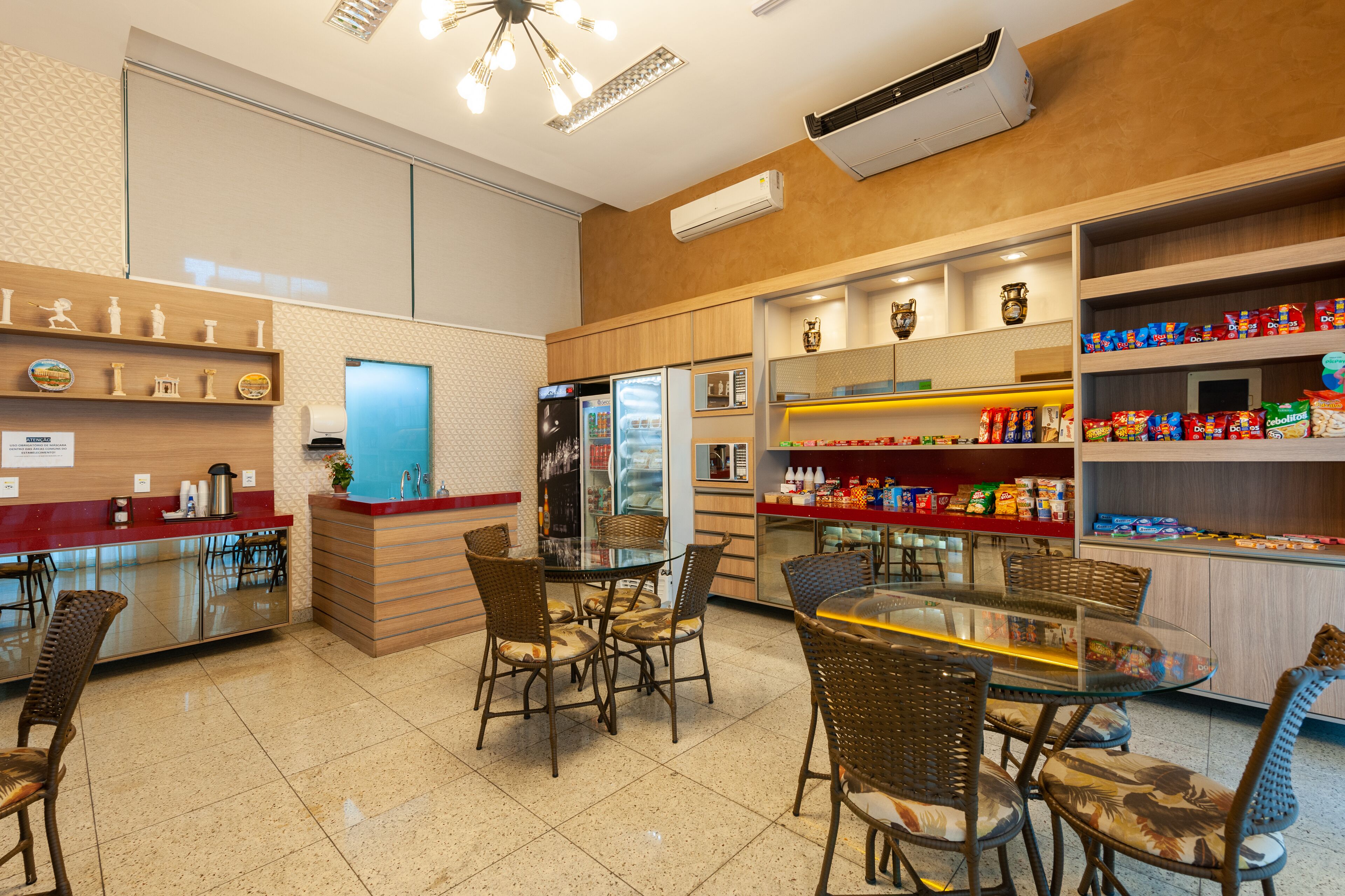 A restaurant with a glass dining area, wicker chairs, a counter with a coffee machine, and shelves stocked with snacks and condiments.